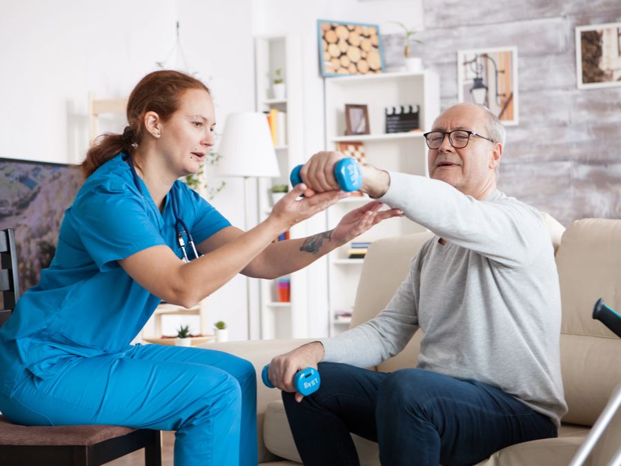 Therapist helping an older man with light dumbbell exercises